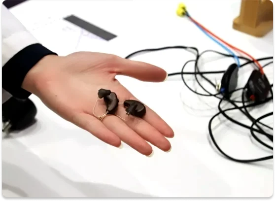 Hearing aids held in an open hand beside testing equipment