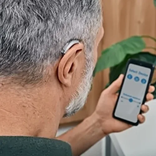 Man adjusting his hearing aid with a phone app